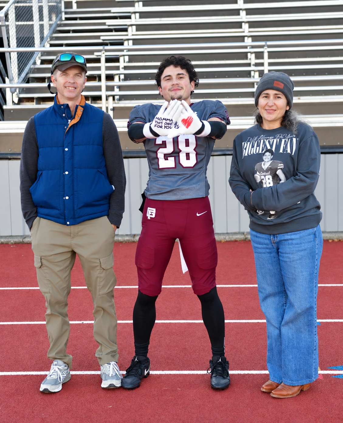 Seifer Trottier in his number 28 uniform, standing with two supporters beside the football field